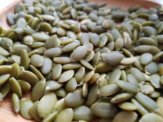 Green pumpkin seeds lie on a wooden plate