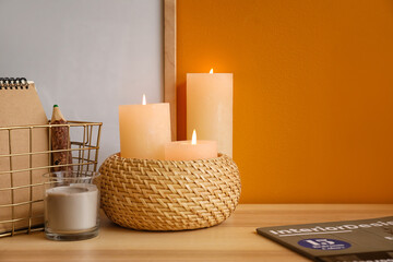 Burning candles and stationery on table against color background