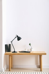 Modern lamp and cup of coffee on table near light wall in room