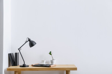 Modern lamp and cup of coffee on table near light wall in room