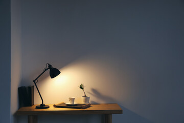 Modern lamp and cup of coffee on table near light wall in room