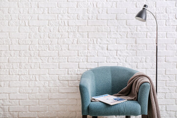 Armchair and lamp near light brick wall in room