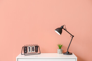 Table with lamp and calendar near color wall in room