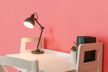 Workplace with glowing lamp on color background