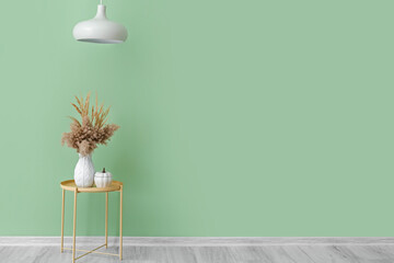 Vase with pampas grass and lamp near color wall in room