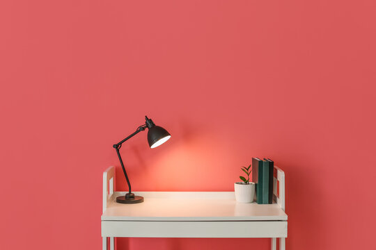 Workplace with glowing lamp on color background