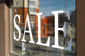 Large white inscription SALE on the glass shop window, outside. Black Friday concept - obrazy, fototapety, plakaty
