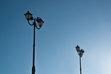 Two vintage street lamps against a clear blue sky during the day