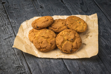 Freshly made oatmeal cookies on paper on a black wooden table.