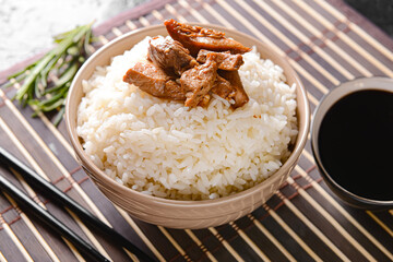Bowl with tasty rice and meat on bamboo mat