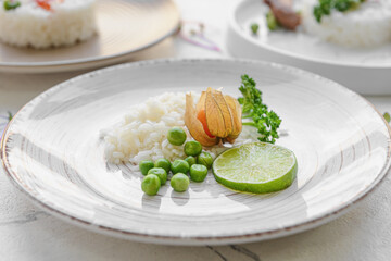 Plate with tasty rice, green peas and lime on light background