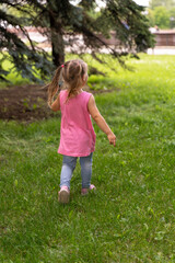 a little girl in a pink tunic walks on the grass in sneakers