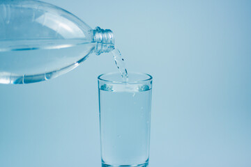 Pouring water into glass on light blue background.