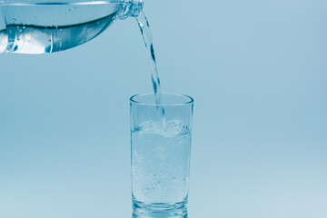 Pouring water into glass on light blue background.