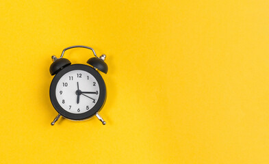 black alarm clock on yellow background. copy space. flat lay