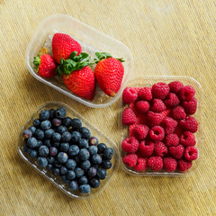 Bought strawberries, raspberries and blueberries in bowls.