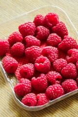 Red raspberries in a plastic transparent bowl.