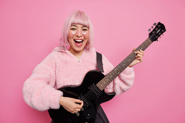Positive fashionable female rock star with pink hairstyle plays acoustic guitar has own music band...
