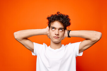 guy in a white t-shirt with curly hair holding his head emotions orange background