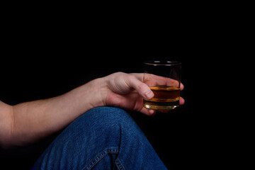 A glass of whiskey in a man's hand on his knee.