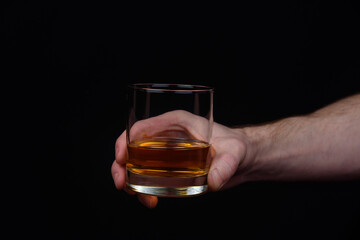 A man's hand holds a glass of whiskey on a black background.
