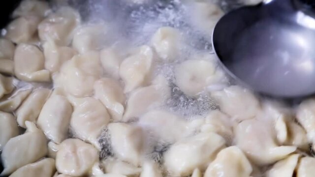 In the process of cooking dumplings, cooked dumplings float on top of boiling water, and someone flips them with a big spoon.
