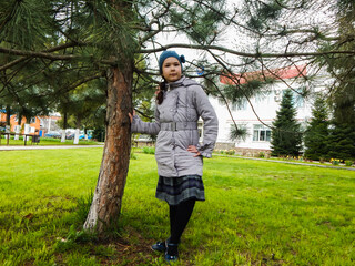 a girl in a green clearing next to a coniferous tree