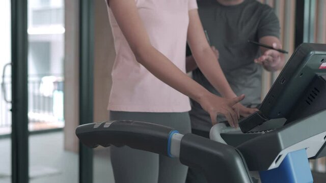 woman is exercising on a treadmill with her trainer advice and record activity details. Exercising in Fitness will be recommended to exercise properly to reduce the risk of injury to your muscles.
