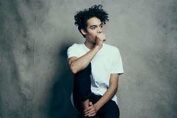 cute guy with curly hair in a white t-shirt sits on chairs studio fashion