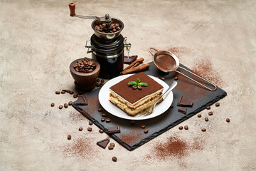Portion of Traditional Italian Tiramisu dessert and hand coffee grinder on grey concrete background