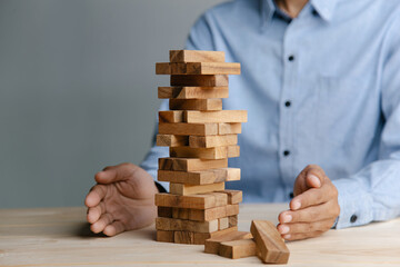 Planning, risk and strategy in business, businessman placing wooden block on a tower.