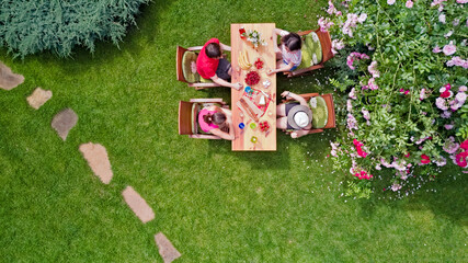 Family and friends eating together outdoors on summer garden party. Aerial view of table with food...