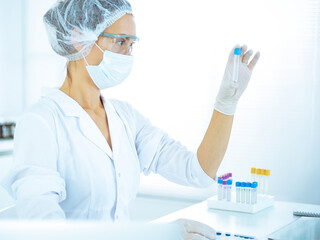 Professional female scientist in protective eyeglasses researching tube with reagents in laboratory toned in blue. Concepts of medicine and science researching