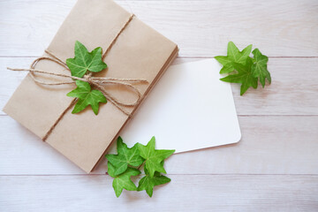 Green ivy leaves with blank letter papers on white wooden background. Botanical concept background. Summer greeting. アイビーの葉と手紙セット、初夏の贈り物、夏のメッセージ背景、夏のガーデニング