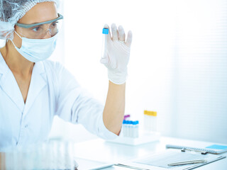 Professional female scientist in protective eyeglasses researching tube with reagents in laboratory...