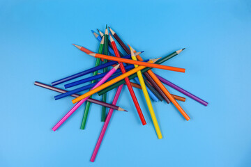 A pile of colored pencils on a blue background. View from above.