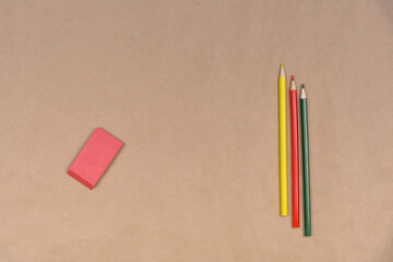 Three colored pencils and one eraser are on craft paper.