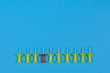 Nine yellow pushpins and one red one lie in a row.
