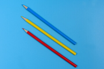 Three colored pencils blue, red and yellow on a light blue background.