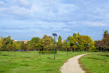 Long alley and many lighting poles activated with attached blue solar panels in Parcul Izvor (Izvor Park) in Bucharest, Romania, with cloudy sky in the background, in a summer day.