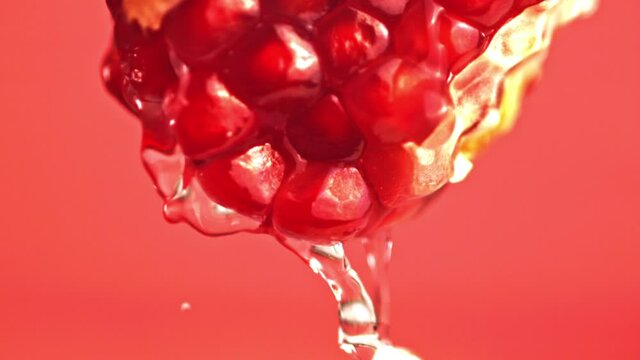 Super slow motion with a piece of pomegranate drains water. On a red background. Filmed on a high-speed camera at 1000 fps. High quality FullHD footage