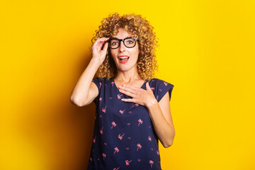 curly young woman in shock, surprised with glasses on a yellow background
