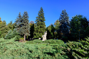 Landscape with statue, green and yellow old large trees and grass in a sunny autumn day in Parcul Carol (Carol Park) in Bucharest, Romania .