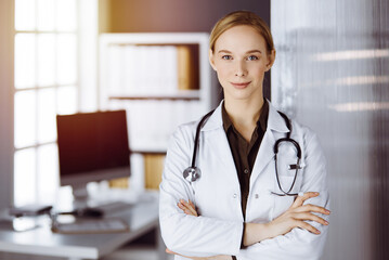 Cheerful smiling female doctor standing in clinic. Portrait of friendly physician woman. Medical service in hospital. Medicine concept