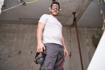 Young builder wearing safety glasses at a construction site. Hearing protection hanging from the...