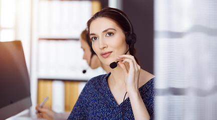 Fototapeta premium Latin american businesswoman talking by headset in office. Call center and diverse people group in business