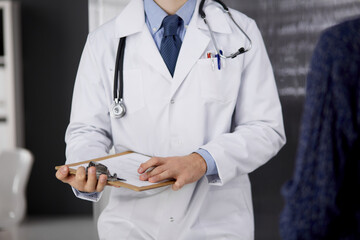 Unknown bearded doctor and patient woman discussing current health examination while sitting in...