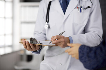 Unknown bearded doctor and patient woman discussing current health examination while sitting in...