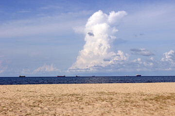 Fototapeta na wymiar Sliver of deep blue ocean with large ships on the horizon against a blue sky with steepling white cloud, seen from a sandy beach