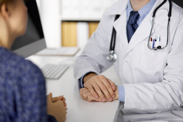 Unknown male doctor and patient woman discussing current health examination while sitting and using tablet computer in clinic, close-up